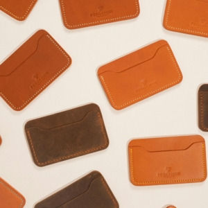Flat lay of stylish brown and orange leather card holders on cream background.